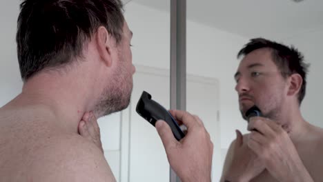 man shaving his beard in front of a mirror with an electrical razor