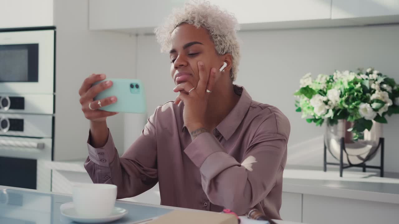 Young outgoing african american woman making video call via phone at breakfast