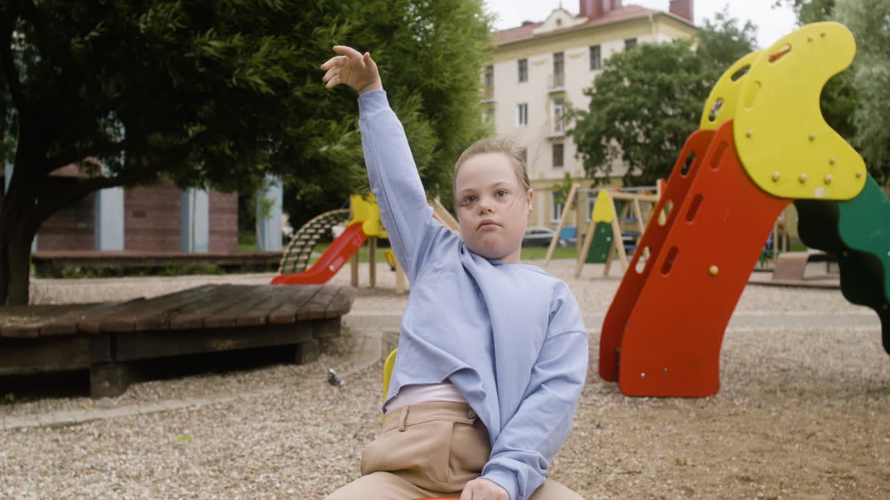 Portrait of a little girl with down syndrome swinging on a wooden rocker in the park on a windy day