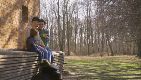 side view of caucasian couple talking with her son while they drinking tea outside a country house. their dog is lying on the ground near them