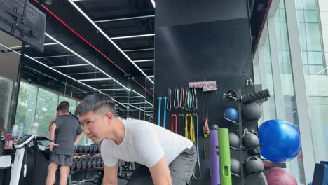 A man performs barbell deadlifts in a modern gym setting, showcasing strength and focus under bright lighting