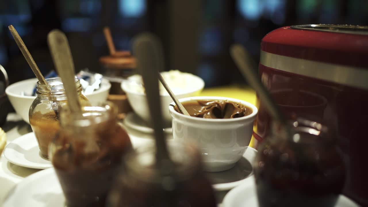 Cozy breakfast table with a variety of sweet jams and spreads in glass jars and bowls, creating a warm and inviting morning atmosphere for a delicious homemade meal