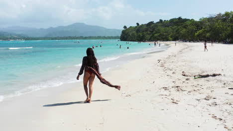 Beachgoer-enjoys-walk-on-white-sand-tropical-paradise,-aerial-crane-down