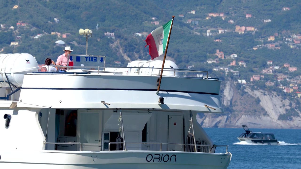 Un traghetto passeggeri bianco naviga lungo la costa della Riviera Ligure sotto la luminosa luce del sole estivo