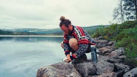 hombre caucásico lavando el cuenco equipo de campamento en el lago