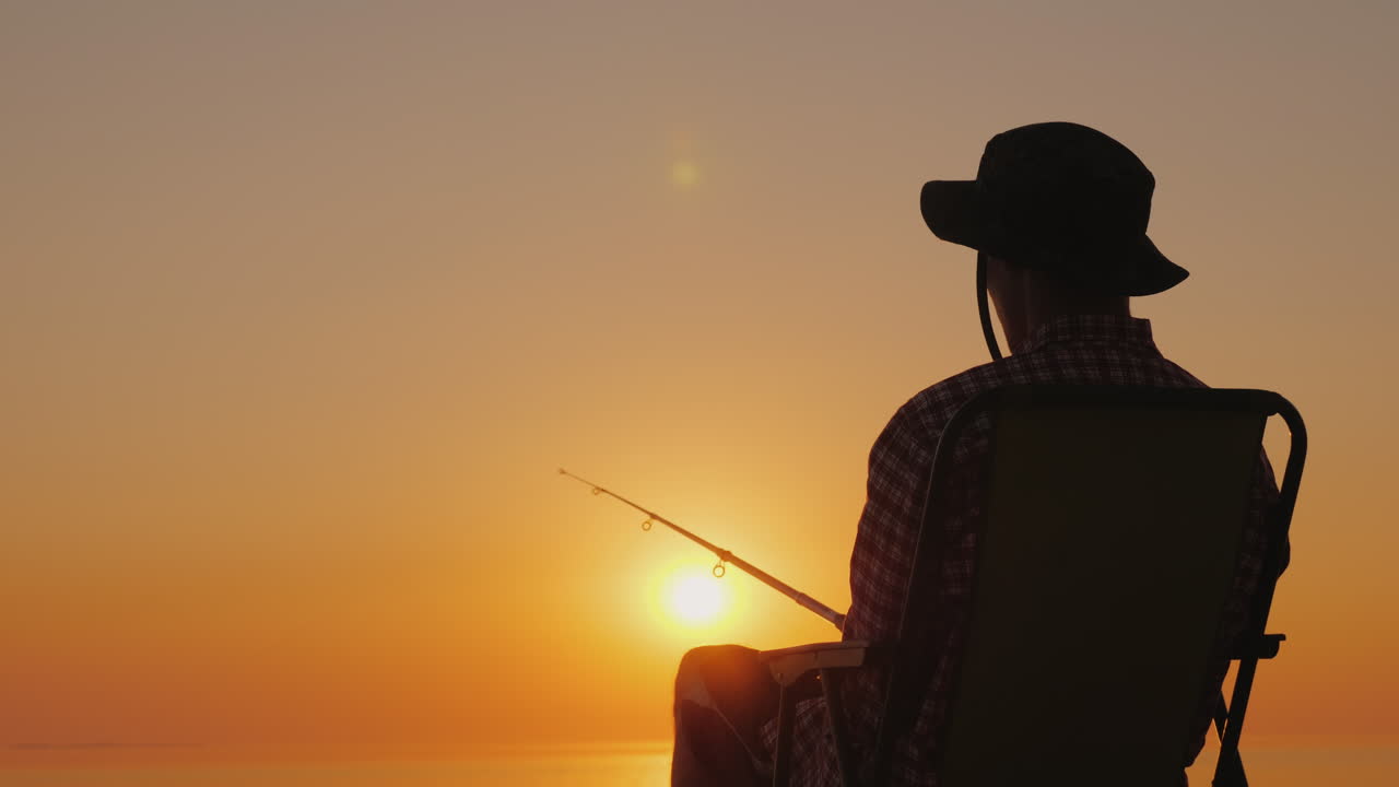 Un giovane è seduto in riva al mare, pescando e rilassandosi all'aria aperta. Video 4K.
