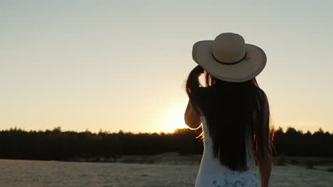 Young-Woman-With-Long-Hair-In-A-Hat-Go-Towards-The-Setting-Sun-Rear-View