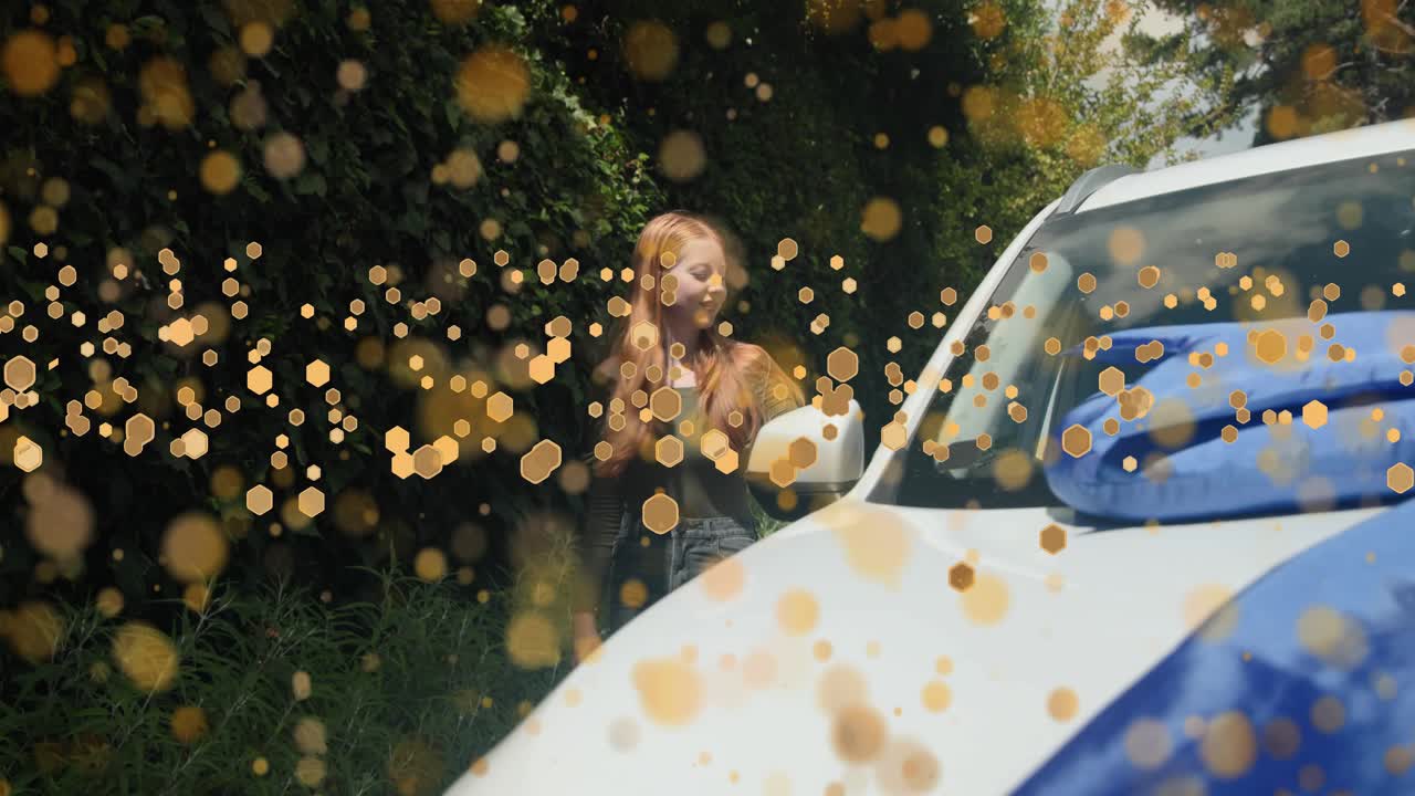 Woman approaching white car, inspecting blue ribbon and hood for automotive reveal while gold bokeh