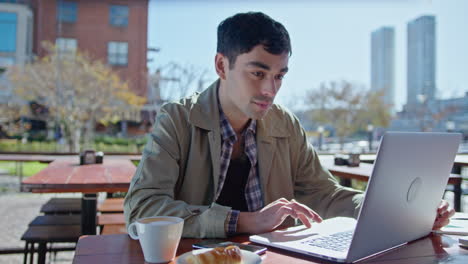 young businessman working on laptop in outdoor cafe
