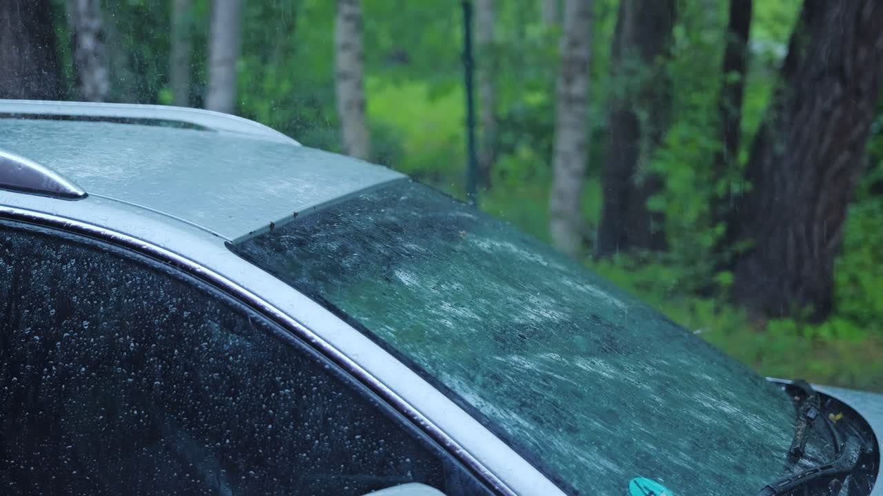 Raindrops burst and streak across windshield and roof in cold slow motion