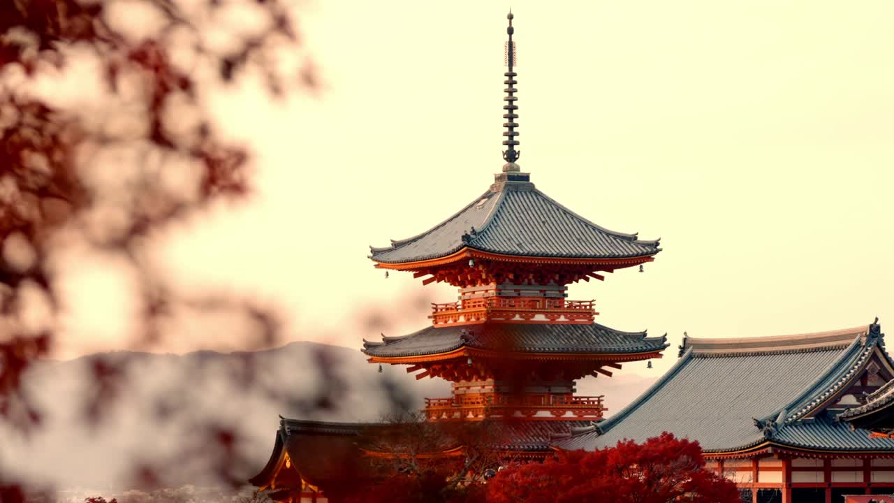 The iconic Kiyomizu-dera Pagoda stands majestically in Kyoto, bathed in the warm hues of sunset and surrounded by vibrant red autumn foliage.