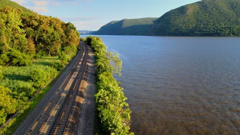 Aerial-drone-footage-of-the-metro-north-Hudson-Line-train-tracks-during-summer-next-to-the-Hudson-river-between-beacon-and-cold-spring,-new-york,-usa