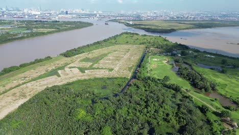 aerial drone view of saigon river winding through green landscape with golf course, forest, and farmland, set against distant skyline and waterways under bright daylight in expanding urban edge