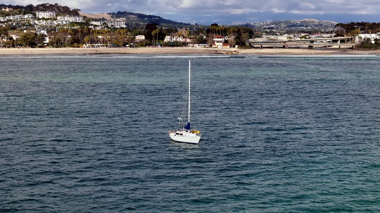 velero anclado en las aguas tranquilas del puerto de dana point con el telón de fondo de la ciudad costera, cielos despejados