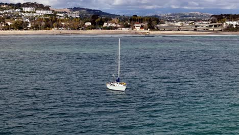 sailboat anchored in calm waters of dana point harbor with coastal town backdrop, clear skies