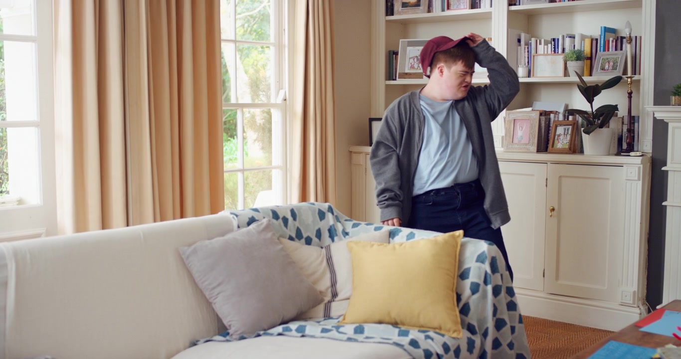 Young Man with Down Syndrome Putting on a Baseball Cap at Home