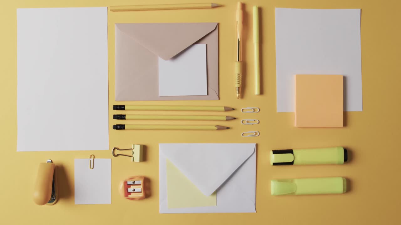 vista aérea de bolígrafos, lápices y artículos de papelería dispuestos sobre un fondo amarillo, en cámara lenta