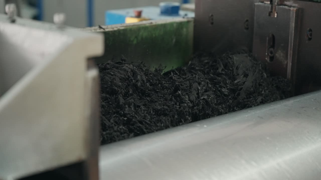 Close up shredded black rubber pieces moving through processing machine in recycling factory