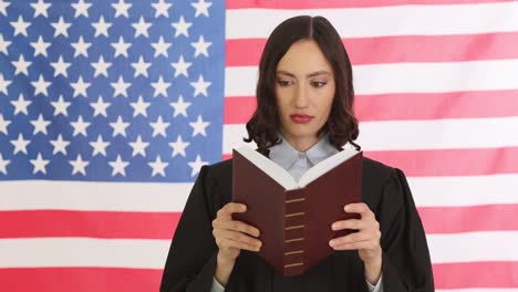 woman in judge's robe reading a book in front of an american flag