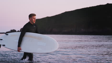 Mann-Im-Neoprenanzug-Mit-Surfbrett,-Als-Er-Aus-Dem-Meer-Geht