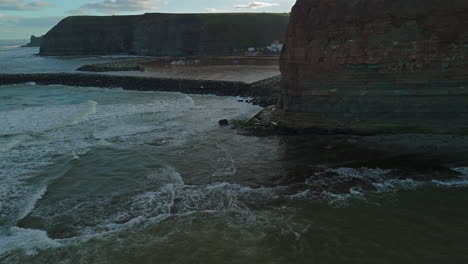 Toma-Baja-Y-Reveladora-De-Un-Dron-De-Staithes-Desde-Detrás-De-Un-Acantilado-Durante-La-Marea-Alta-En-El-Reino-Unido