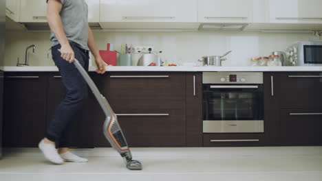 Caring-man-cleaning-floor-with-vacuum-machine-at-modern-kitchen.