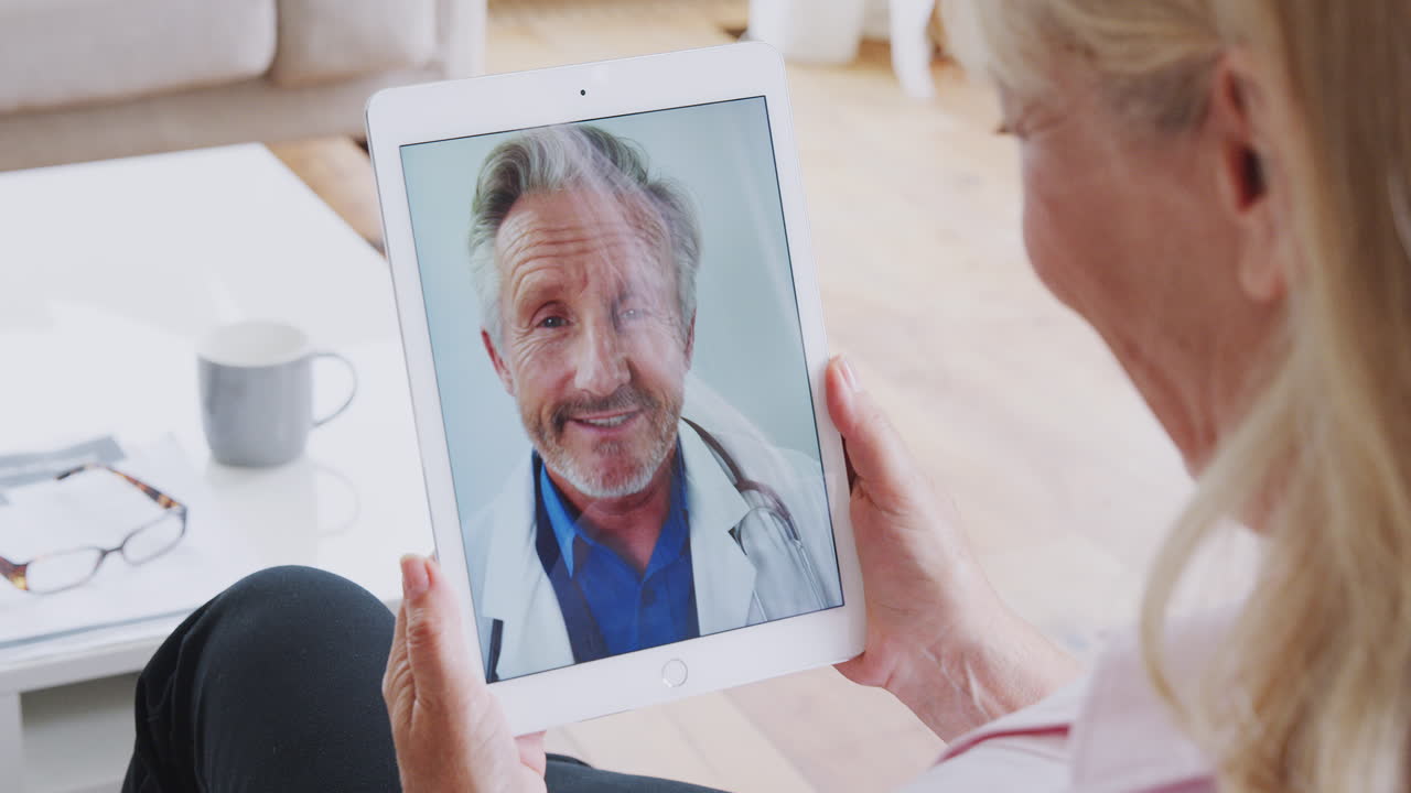 Donna matura che ha consultazione online con il medico a casa sulla tavoletta digitale