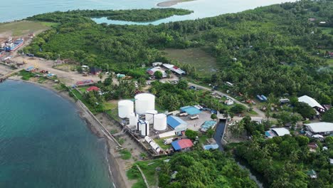 aerial pullback of coastal fuel depot facilities and warehouse at lush tropical island of catanduanes, philippines during daytime