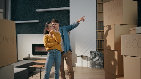 spouses standing new living room purchased house discussing interior together.