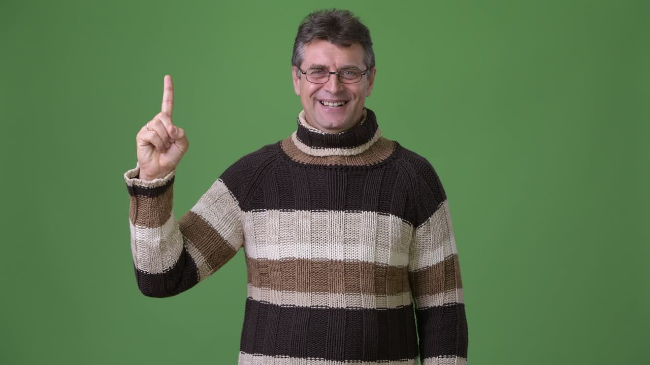 hombre guapo maduro con suéter de cuello alto contra un fondo verde