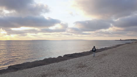 Hombre-Caminando-En-Una-Playa-De-Arena-En-Ibiza-Durante-La-Puesta-De-Sol