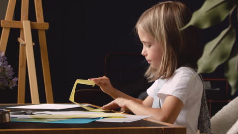 side view of blonde girl building geometrics shapes with cardboard sitting at desk 1