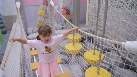 toddler girl playing on indoor rope bridge playground