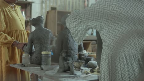 artists sculpt clay figures in a busy studio, surrounded by tools and materials