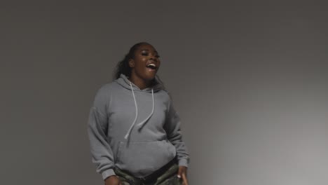 studio portrait shot of young woman wearing hoodie dancing with low key lighting against grey background 1