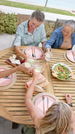 vertical video: senior women toasting drinks, enjoying meal together at outdoor dining table