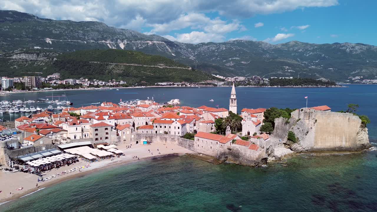 Citadel Budva medieval fortress and stone houses with terracotta roofing in old town on the Adriatic coastline with mountains in backdrop, drone shot