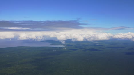 Ein-Blick-Aus-Einem-Flugzeug-Zeigt-Eine-üppige-Tropische-Waldinsel,-Die-Von-Weißen-Wolken-Umgeben-Ist