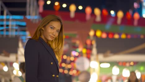 attractive young woman brushes her hair back and smiles at the camera under the night lights in the city