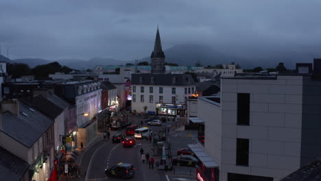 Forwards-fly-above-street-and-square-in-town-at-dusk.-Cars-driving-on-road.-Illuminated-house-facades.-Killarney,-Ireland-in-2021