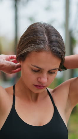 Close-up view of young fair lady packing her hair in a game park, preparing for an outdoor activity, adjusting her ponytail, and looking ahead, outdoors in a park setting