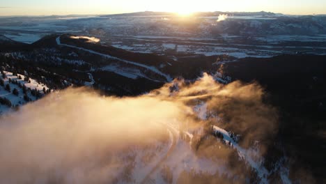 winter sunset above mountain landscape, flying above light clouds and snow capped landscape