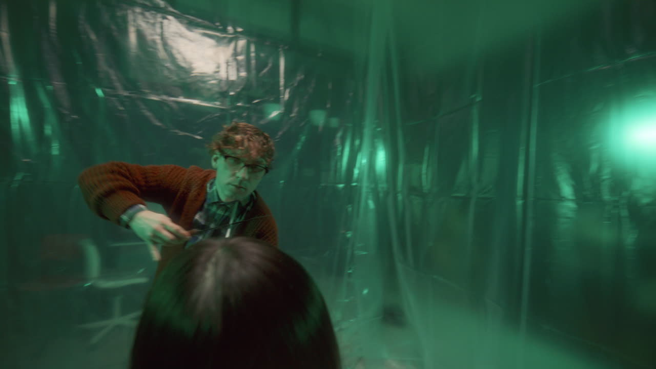 un asesino psicótico con cuchillos bailando alrededor de un rehén atado a una silla en una habitación oscura.