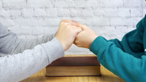 a man praying alone and then together holding hands with a bible on a table and holdimg hands