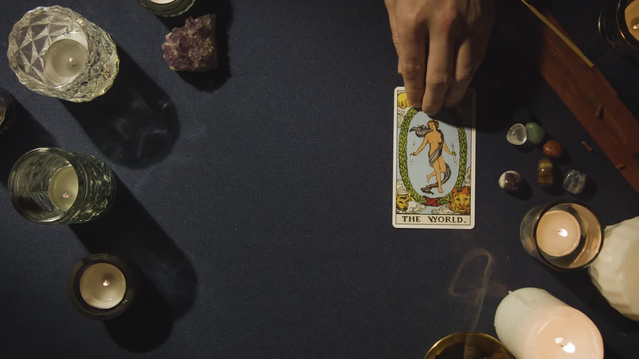 toma aérea de una persona que da una lectura de cartas del tarot colocando la carta del mundo en la mesa 1