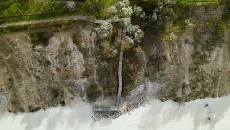 Vista-Aérea---Escalera-Para-Bajar-Del-Acantilado-Y-Gente-Caminando-A-Lo-Largo-Del-Mar-Báltico-Al-Pie-De-Un-Acantilado-En-Chlapowo,-Polonia