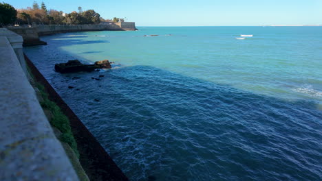 calm blue waters next to a stone sea wall, with a view of distant shoreline