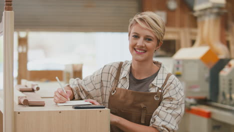 retrato de una carpintero aprendiz sonriente que trabaja en un taller de muebles tomando notas