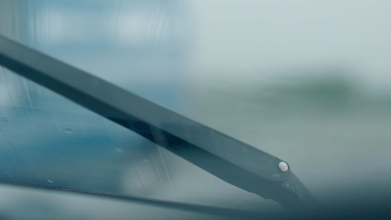 closeup black windshied wiper cleans raindrops from glass
