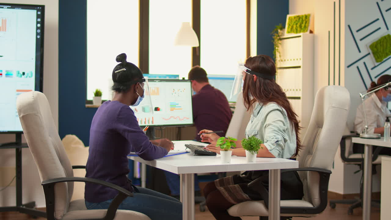 Multi ethnic employees with visor sitting at desk analysing statistics